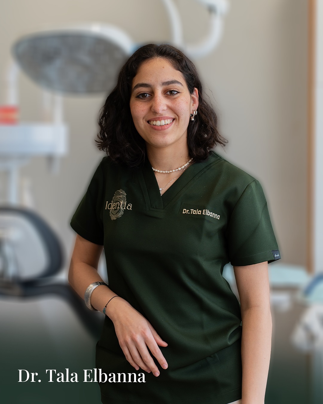 Portrait of Dr. Tala Elbanna in green Identia scrubs against a soft clinic background.