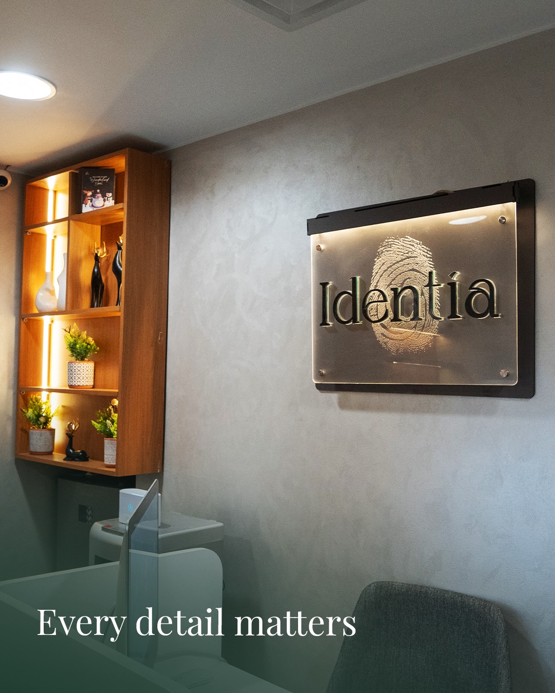 Brushed-metal Identia plaque beside a backlit walnut display cabinet.