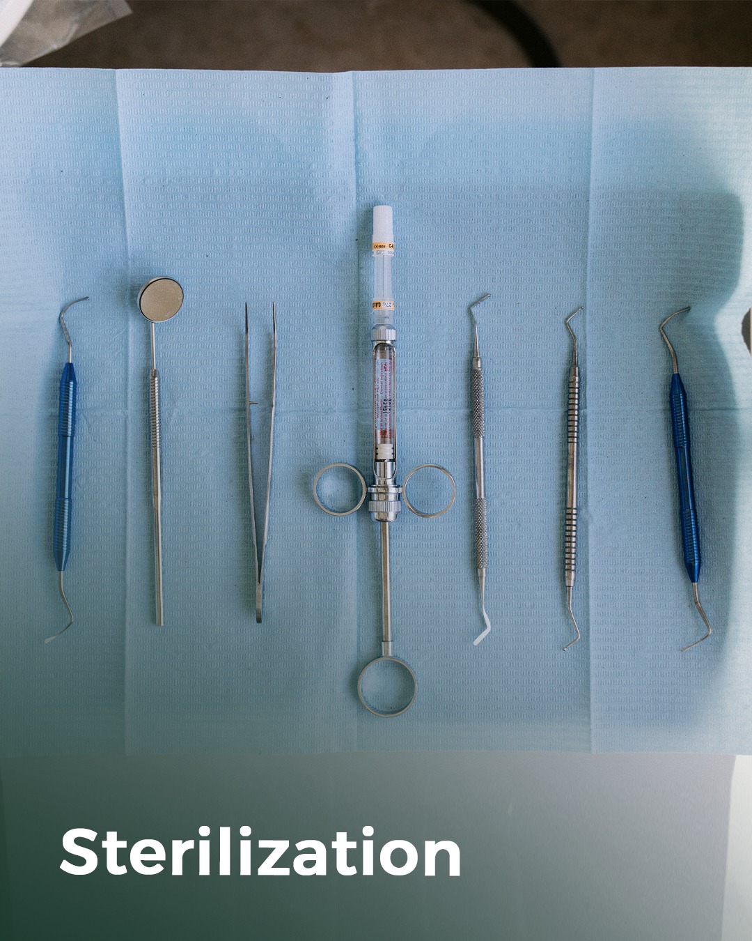 Flat-lay of sterile instruments and a syringe on clinical-blue drape.